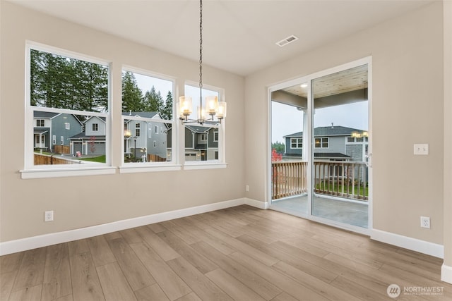 unfurnished dining area with baseboards, visible vents, wood finished floors, and a notable chandelier