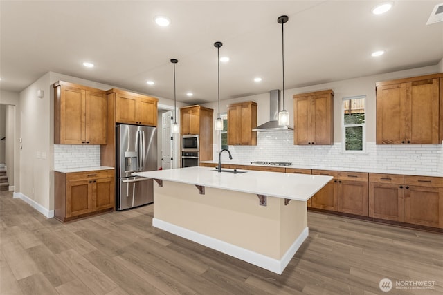 kitchen with brown cabinetry, wall chimney exhaust hood, appliances with stainless steel finishes, and a sink