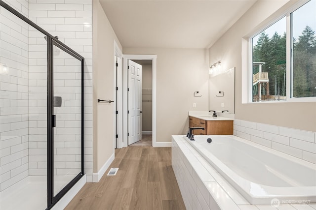 bathroom featuring wood finished floors, a bath, vanity, visible vents, and a stall shower