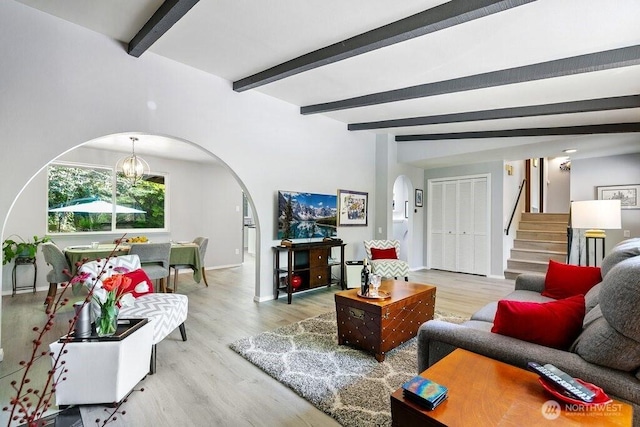 living room featuring stairs, wood finished floors, beam ceiling, baseboards, and arched walkways