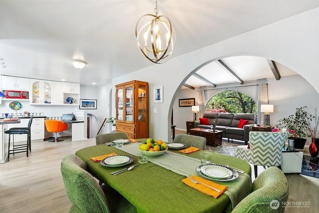 dining area featuring light wood-style floors, arched walkways, and an inviting chandelier