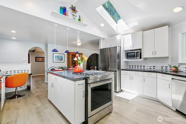 kitchen featuring dark countertops, appliances with stainless steel finishes, arched walkways, light wood-type flooring, and lofted ceiling with skylight