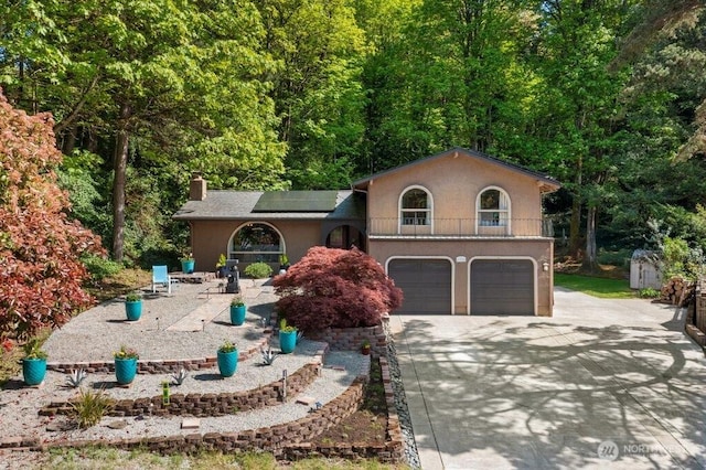 view of front of house featuring a chimney, solar panels, concrete driveway, an attached garage, and stucco siding