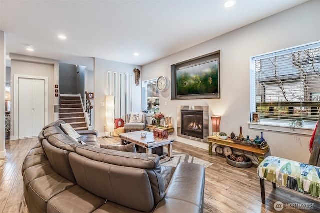 living area with a glass covered fireplace, wood finished floors, recessed lighting, and stairs