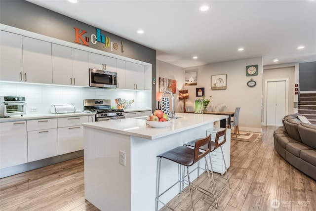 kitchen featuring a sink, light wood-style floors, a kitchen bar, appliances with stainless steel finishes, and recessed lighting