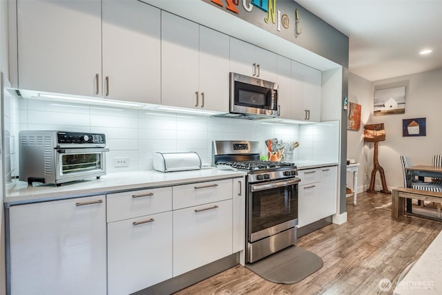 kitchen with appliances with stainless steel finishes, a toaster, light wood finished floors, and light countertops
