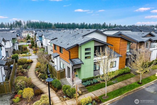 modern home with a residential view, a balcony, a shingled roof, and fence