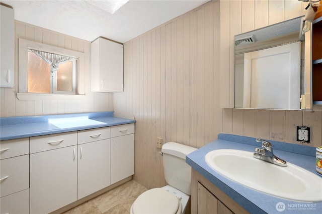 bathroom with toilet, visible vents, wood walls, and vanity