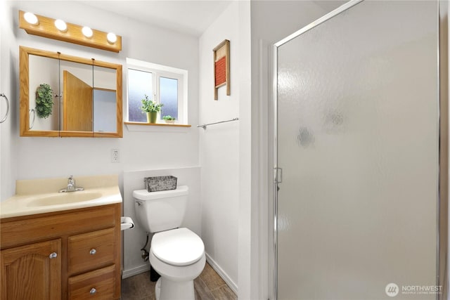 bathroom with toilet, a shower stall, vanity, and baseboards