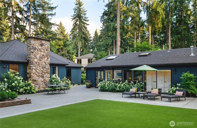 rear view of property with a patio area, a lawn, roof with shingles, and a chimney