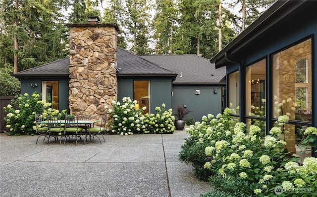 rear view of property featuring a patio area, a shingled roof, a chimney, and outdoor dining space