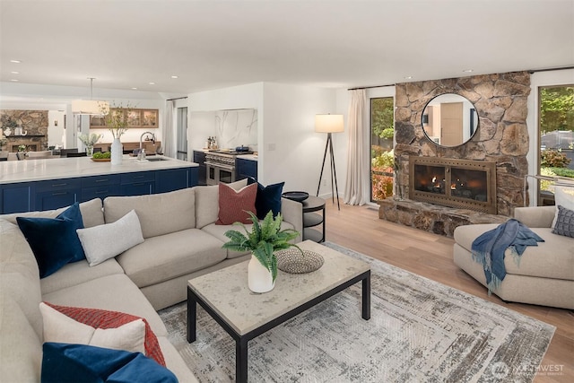 living area featuring light wood-type flooring, a chandelier, a stone fireplace, and recessed lighting