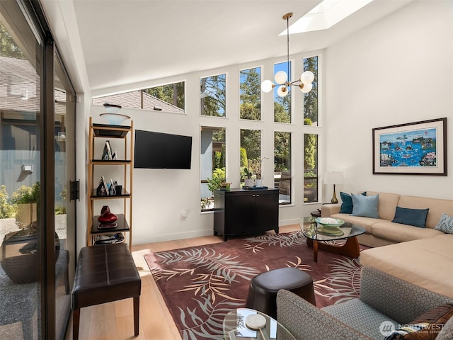 living area featuring plenty of natural light, a skylight, wood finished floors, baseboards, and high vaulted ceiling