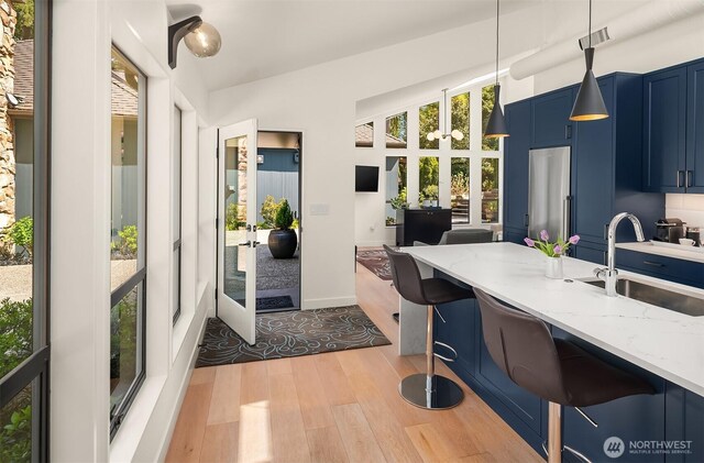 kitchen featuring a sink, blue cabinetry, light wood-style floors, french doors, and light stone counters
