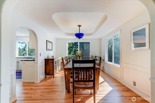 dining area with arched walkways, light wood-style flooring, and a tray ceiling