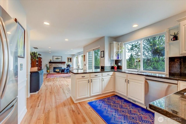kitchen featuring stainless steel appliances, dark stone countertops, a sink, a fireplace, and light wood-style flooring