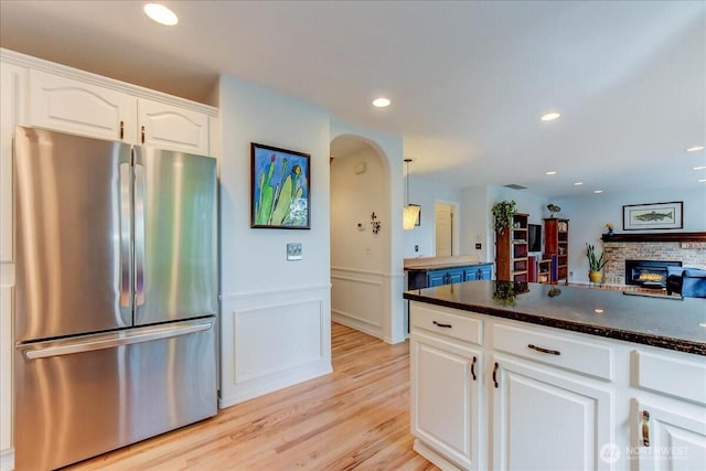 kitchen with white cabinets, arched walkways, dark countertops, freestanding refrigerator, and a fireplace