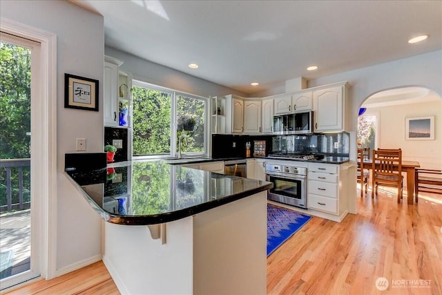 kitchen featuring decorative backsplash, light wood-style floors, arched walkways, stainless steel appliances, and a peninsula