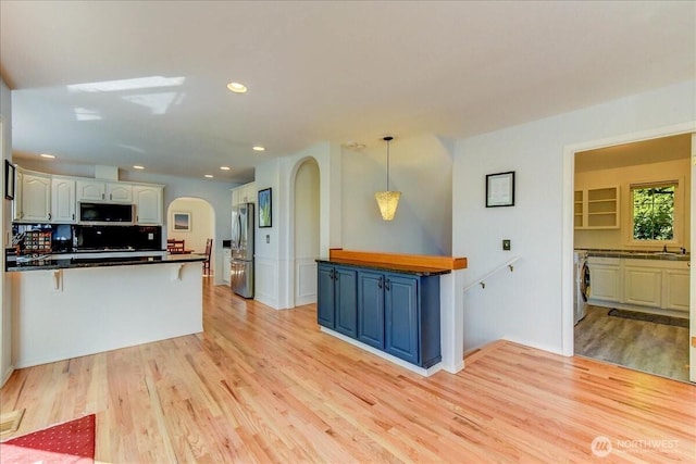 kitchen with dark countertops, arched walkways, light wood-style flooring, appliances with stainless steel finishes, and washer / clothes dryer