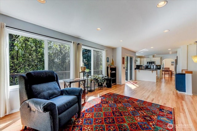 living area featuring recessed lighting, arched walkways, light wood-type flooring, and plenty of natural light