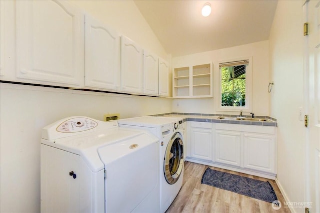 laundry room featuring cabinet space, independent washer and dryer, light wood-type flooring, and a sink