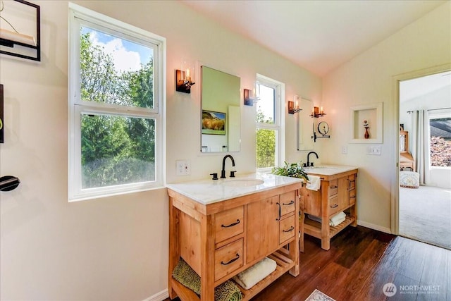 ensuite bathroom with lofted ceiling, wood finished floors, connected bathroom, a sink, and two vanities
