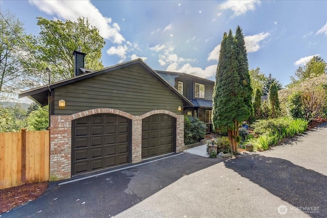view of front facade featuring a chimney, fence, an attached garage, driveway, and brick siding
