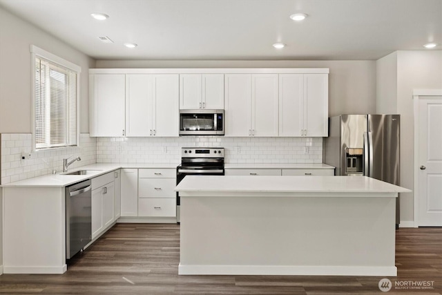 kitchen with a kitchen island, appliances with stainless steel finishes, a sink, white cabinets, and dark wood-style floors