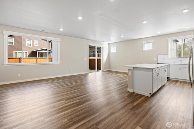 kitchen featuring decorative backsplash, wood finished floors, baseboards, a center island, and light countertops