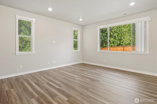 unfurnished room featuring baseboards, visible vents, a wealth of natural light, and wood finished floors