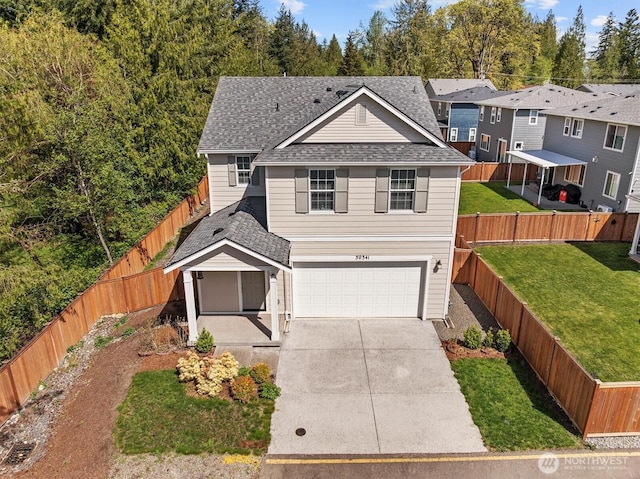 traditional-style house with a garage, a front lawn, a fenced backyard, roof with shingles, and driveway
