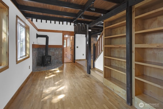 unfurnished living room featuring beamed ceiling, wood finished floors, a wood stove, and wooden ceiling