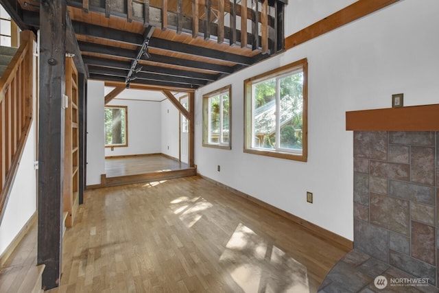 unfurnished living room with beamed ceiling, baseboards, and wood finished floors