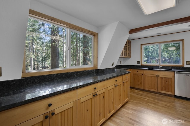 kitchen with light wood finished floors, a sink, dark stone countertops, glass insert cabinets, and dishwasher