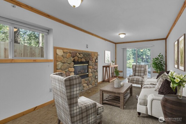 living area featuring plenty of natural light, ornamental molding, a stone fireplace, and baseboards