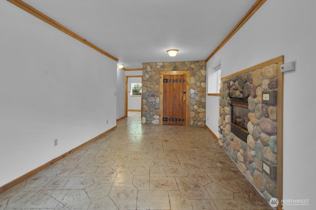 foyer entrance with crown molding, stone finish flooring, baseboards, and a glass covered fireplace