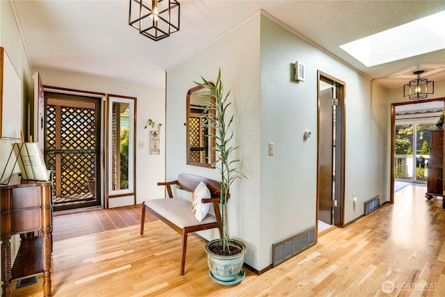 foyer with baseboards, wood finished floors, a skylight, visible vents, and ornamental molding
