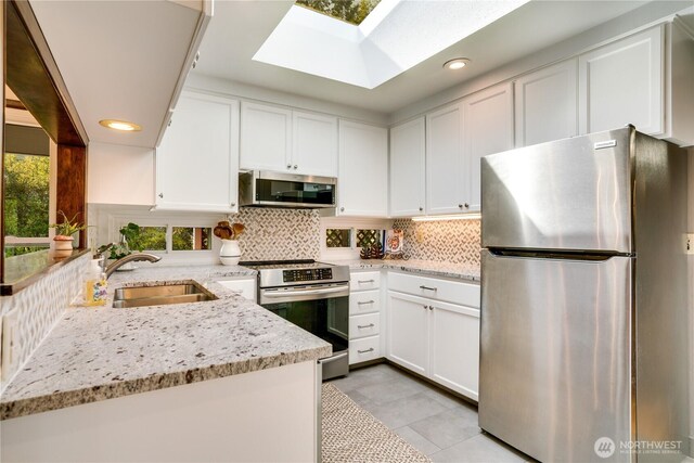 kitchen featuring a sink, stainless steel appliances, white cabinetry, backsplash, and a skylight