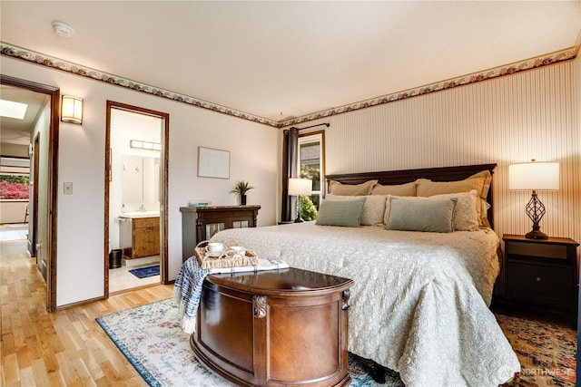 bedroom featuring light wood-style floors, baseboards, ensuite bathroom, and a sink