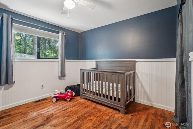 unfurnished bedroom featuring visible vents, a crib, wood finished floors, and a wainscoted wall