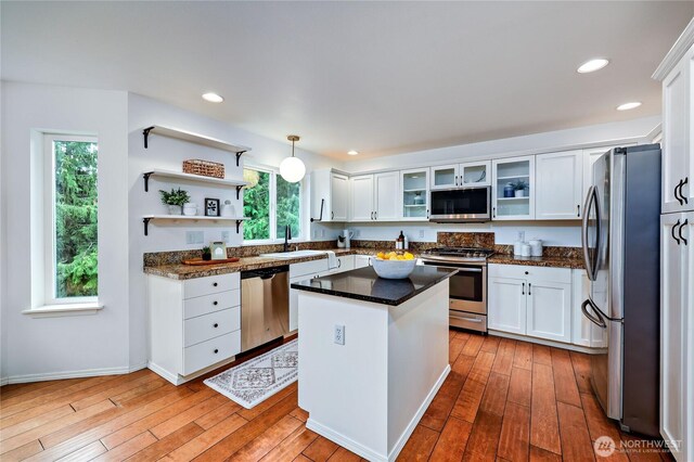 kitchen with a center island, white cabinets, a sink, light wood finished floors, and stainless steel appliances