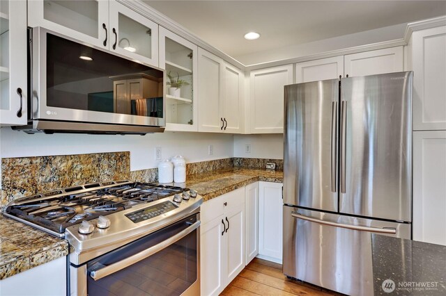 kitchen with light wood finished floors, glass insert cabinets, stainless steel appliances, recessed lighting, and white cabinetry