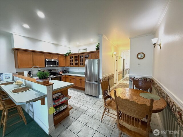 kitchen featuring appliances with stainless steel finishes, brown cabinets, ornamental molding, a peninsula, and glass insert cabinets