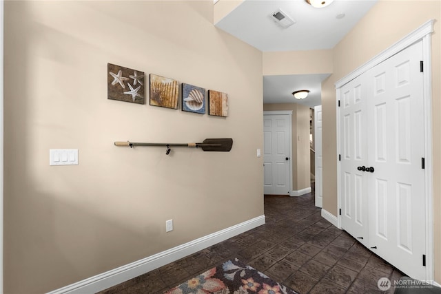 hall with visible vents, stone finish flooring, and baseboards