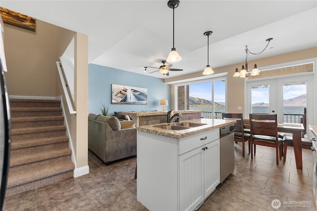 kitchen featuring white cabinets, stainless steel dishwasher, a sink, ceiling fan with notable chandelier, and hanging light fixtures
