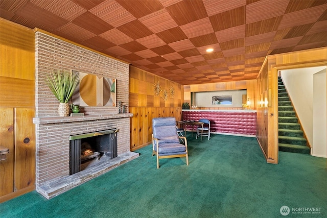 living area featuring a brick fireplace, wood walls, carpet floors, and stairway