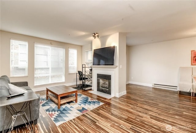 living area with a baseboard heating unit, a fireplace with flush hearth, baseboards, and plenty of natural light