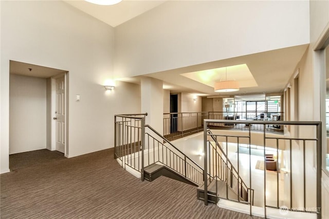 hall featuring a towering ceiling, carpet floors, and an upstairs landing