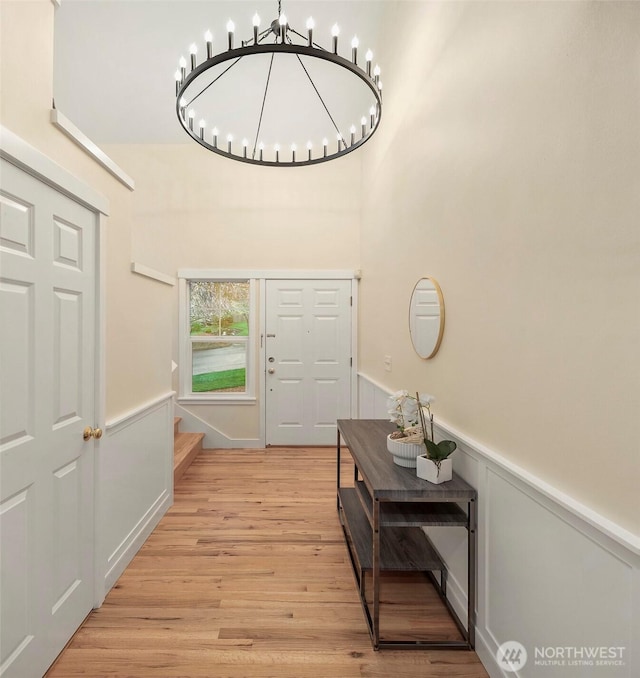 foyer entrance with a wainscoted wall, an inviting chandelier, and light wood-style flooring
