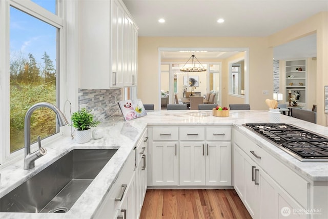kitchen featuring light stone counters, a sink, stainless steel gas stovetop, light wood-style floors, and white cabinets
